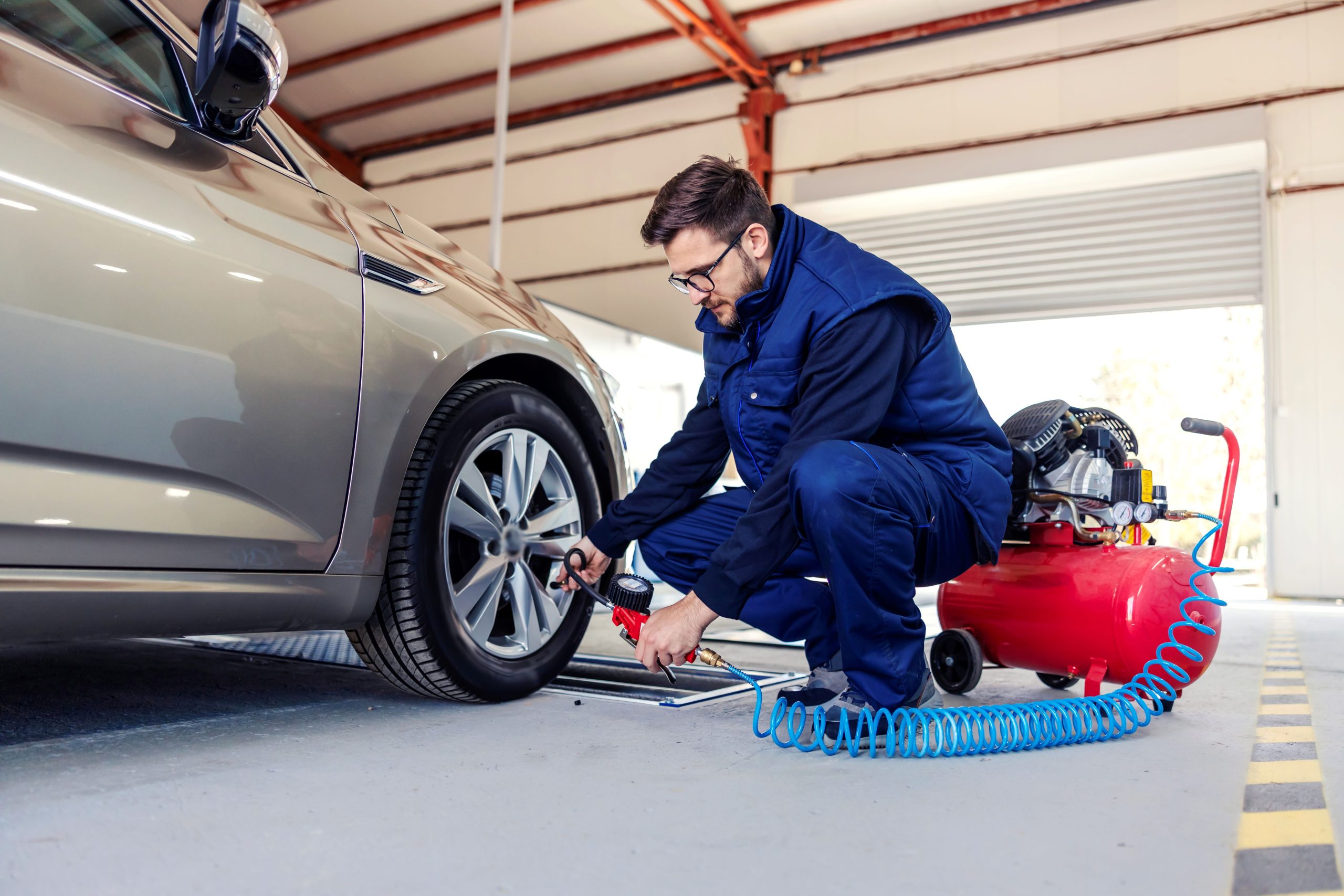 A technician inflating a car tire using an air compressor in a service garage.