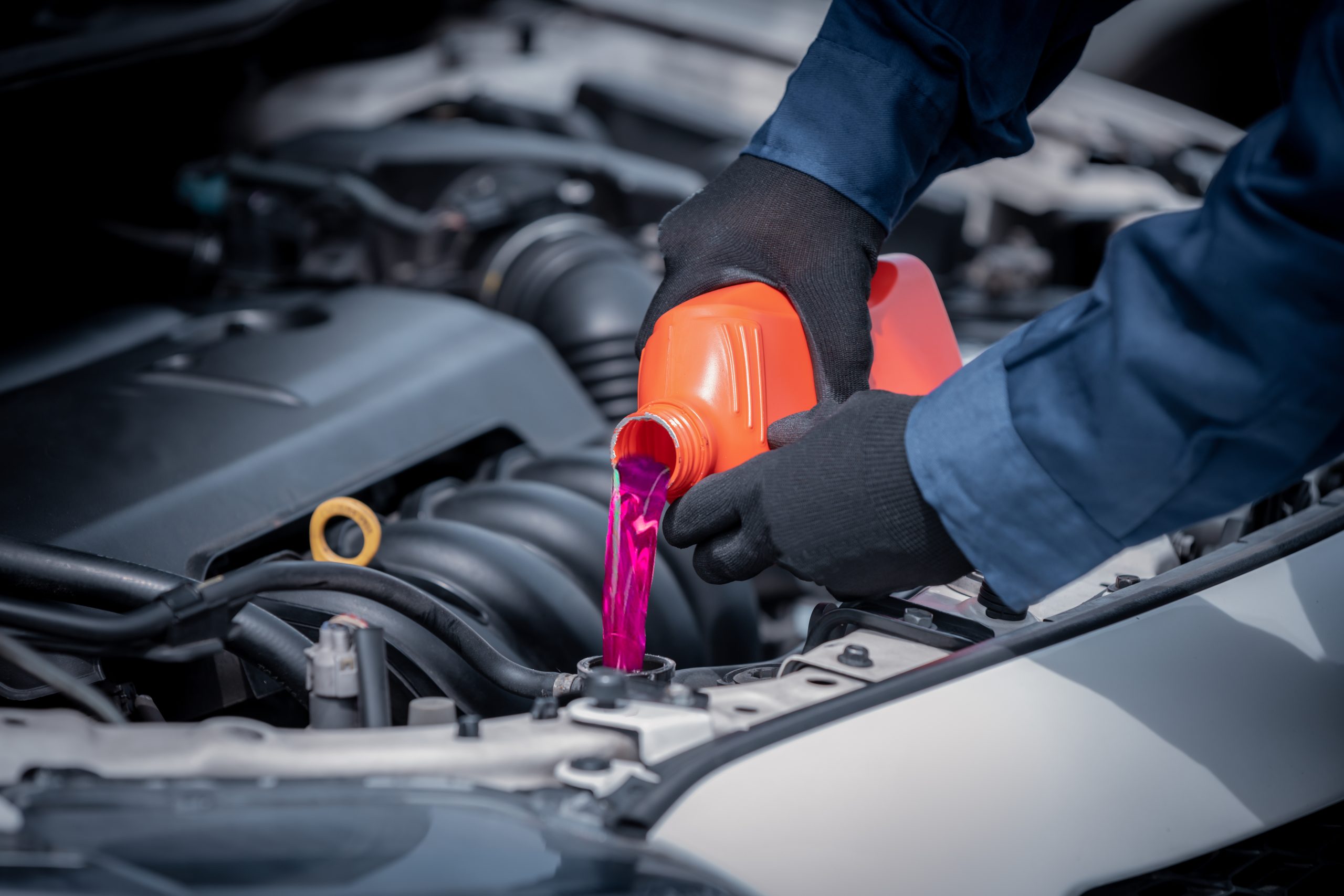 A person pouring coolant into a car engine, ensuring proper maintenance for vehicle performance.