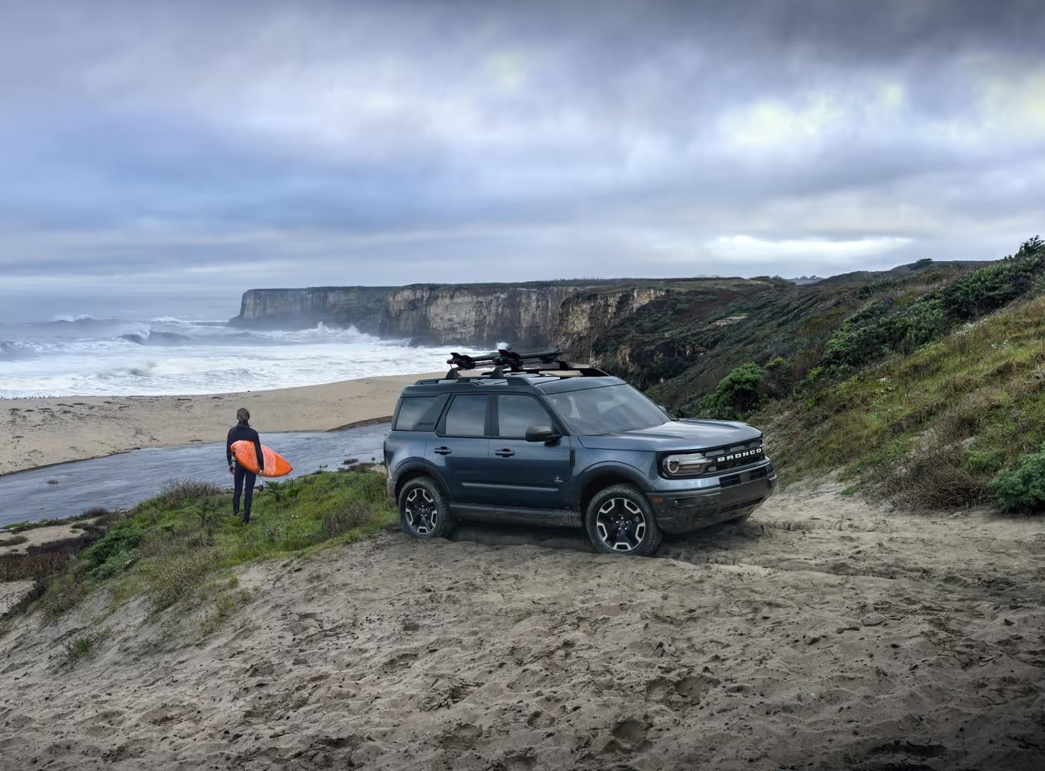 Ford Bronco parked by the water with a surfer looking out a the waves